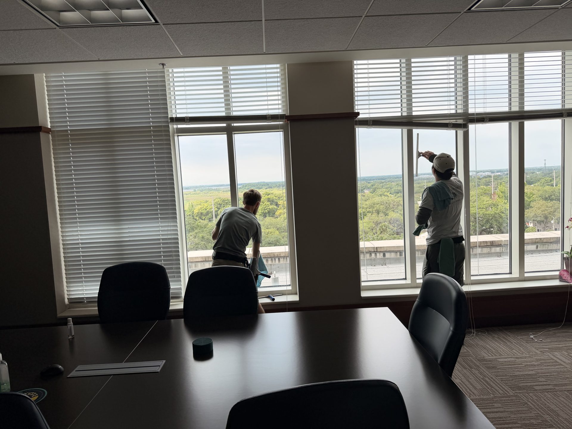 Two technicians cleaning the interior windows of a corporate boardroom