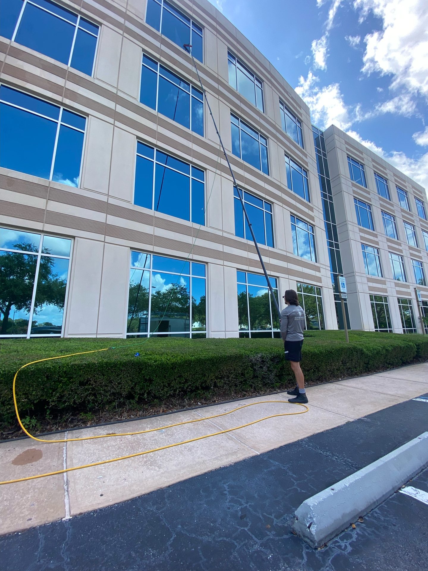 Technician cleaning third-story office windows with an extended water-fed pole