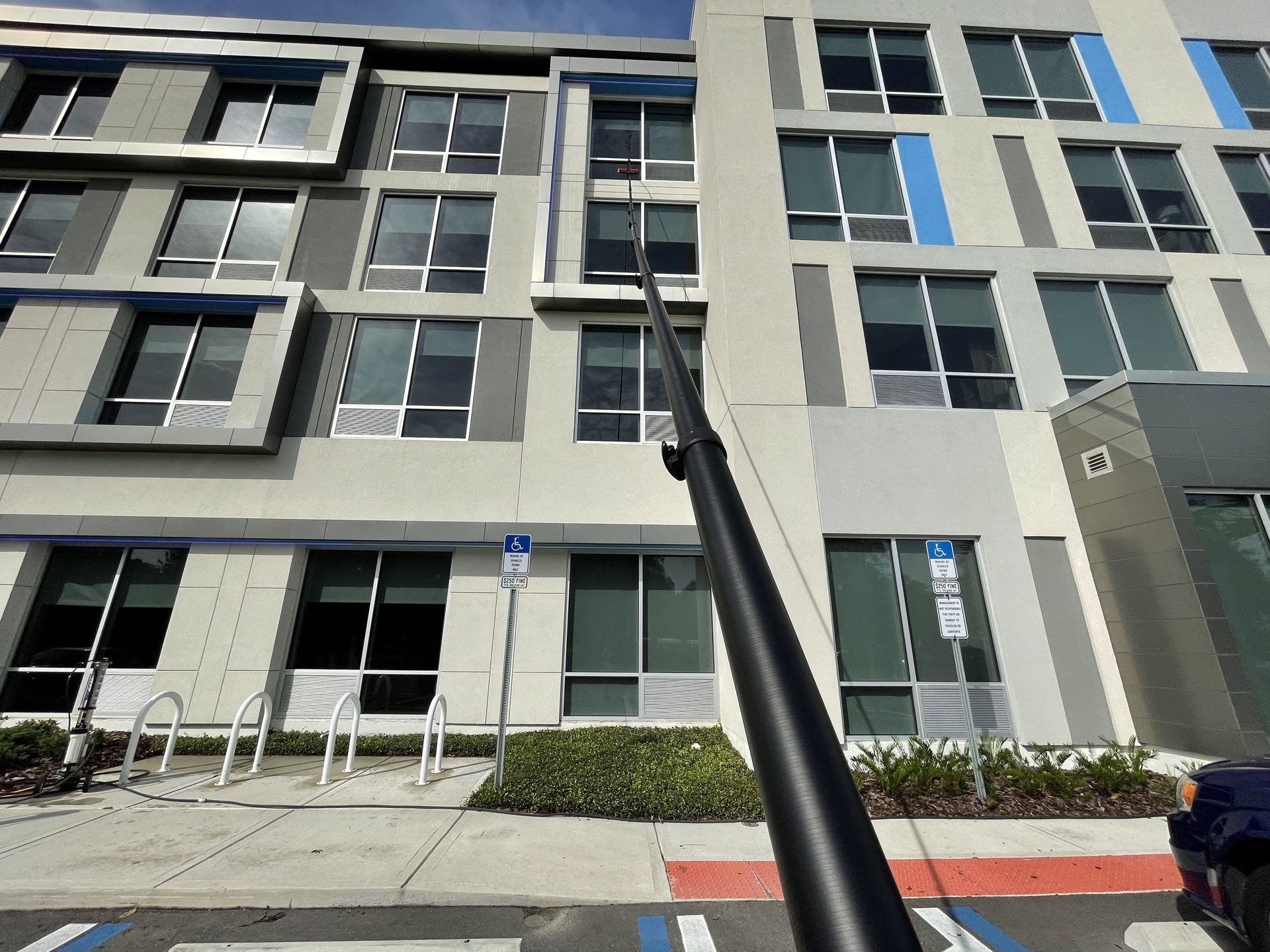Water-fed pole cleaning the windows of a four-story commercial building, from the technician's point of view