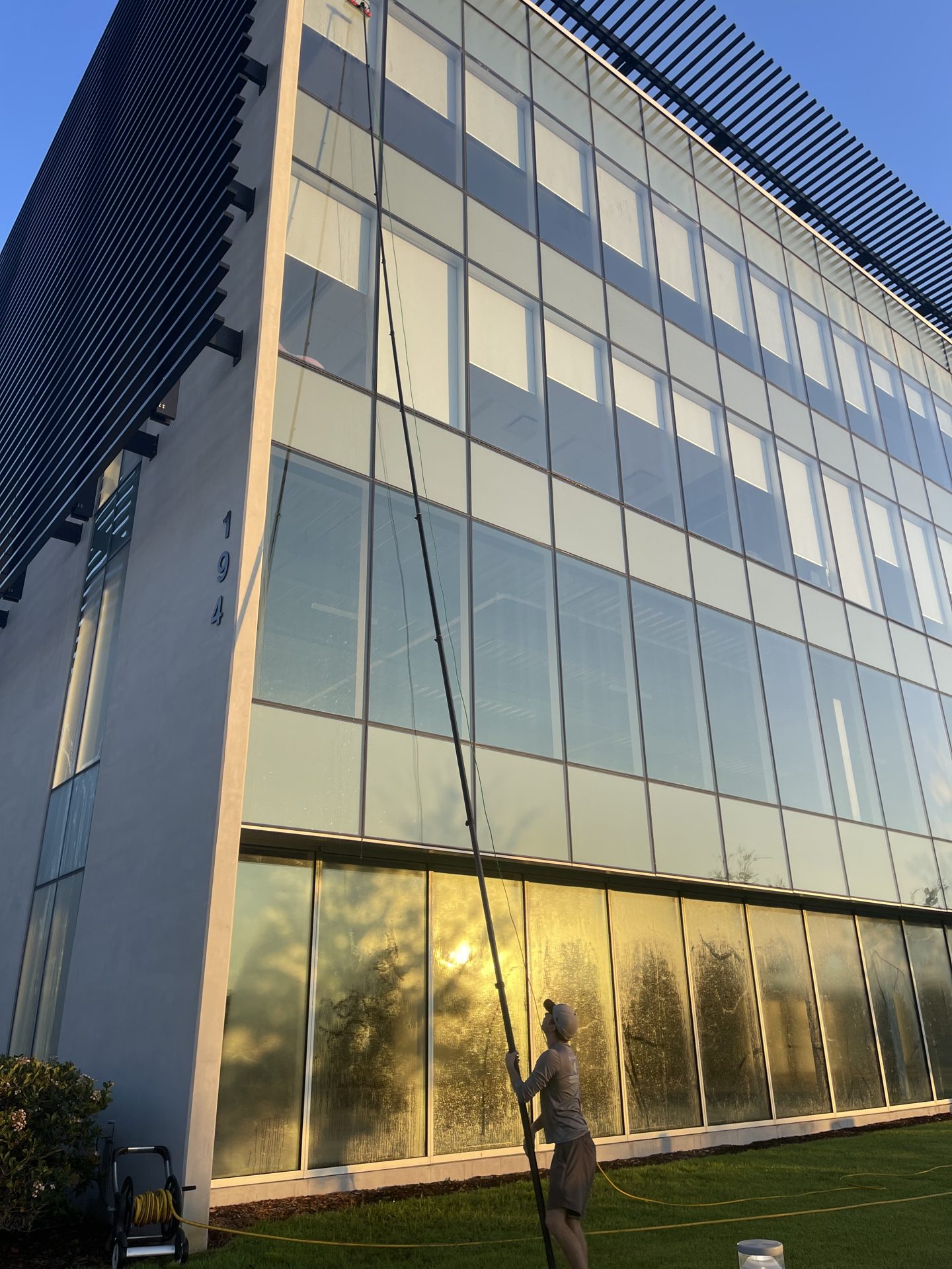 Technician cleaning fourth-story windows of a glass office building with a water-fed pole