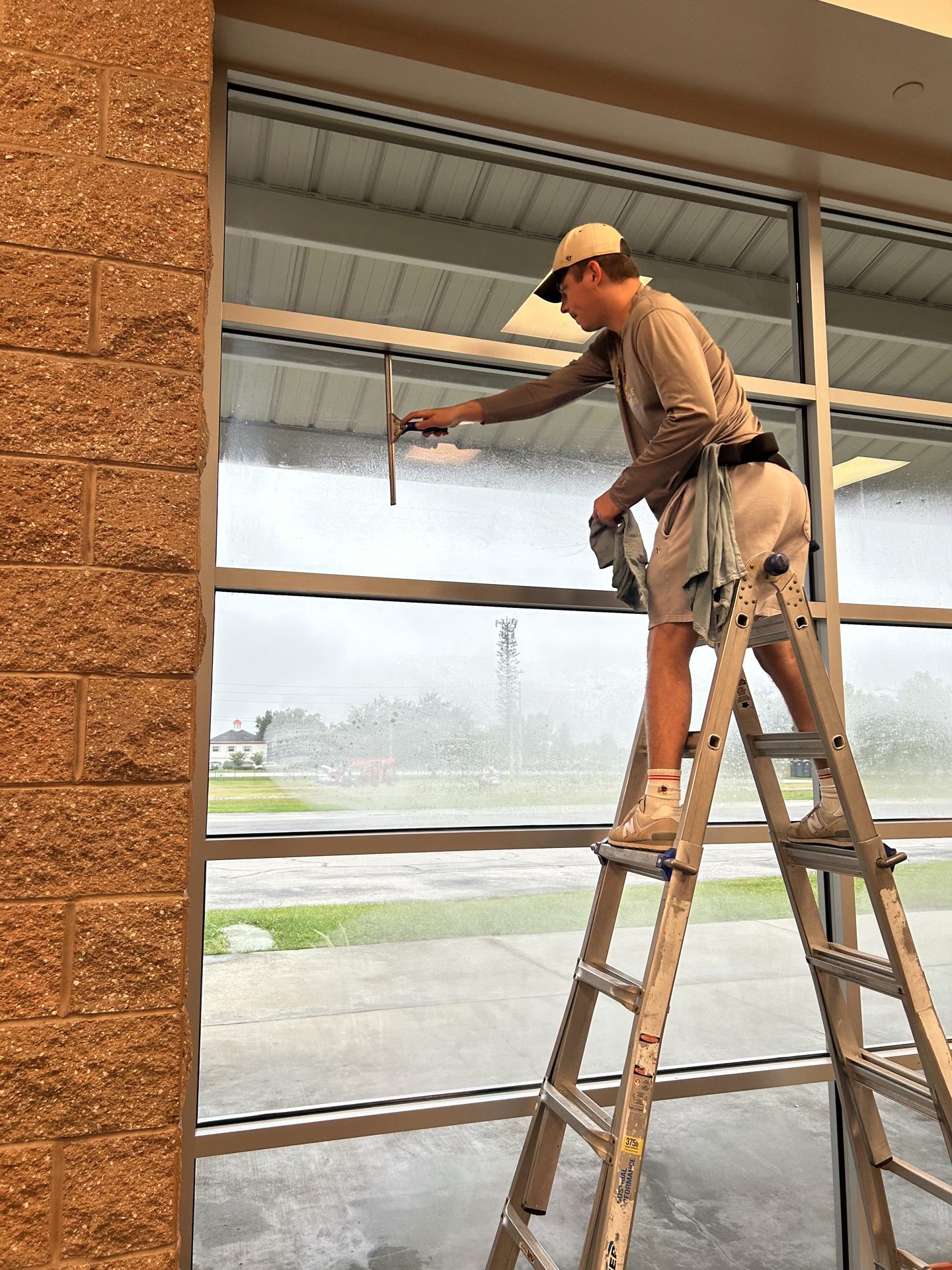 Technician on a ladder squeegee-cleaning the tall windows of a showroom