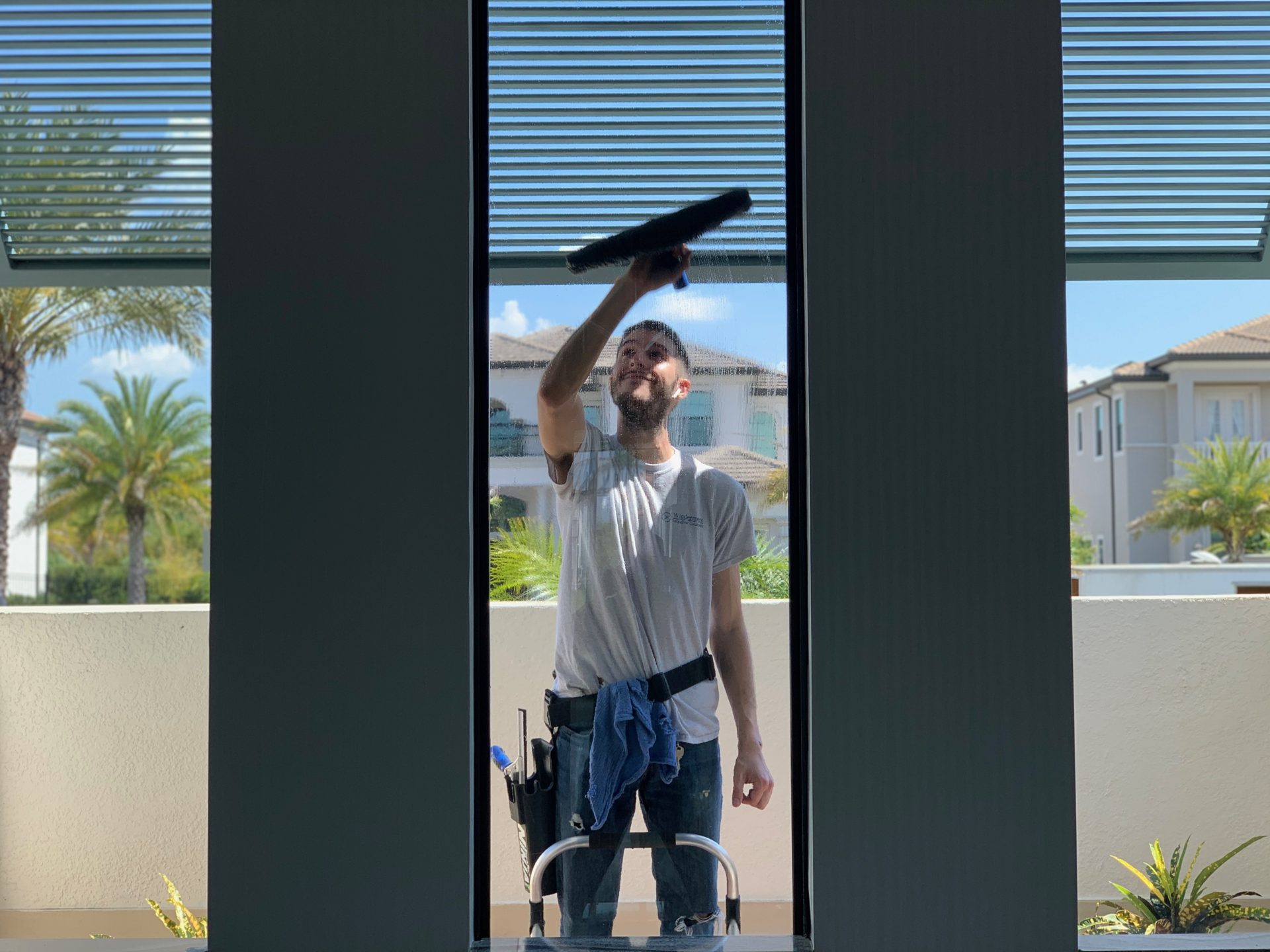 Technician on a ladder cleaning tall interior windows
