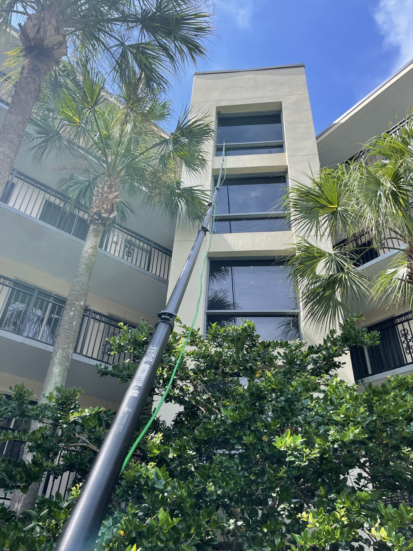 Technician cleaning third-floor windows of a condo building with a water-fed pole