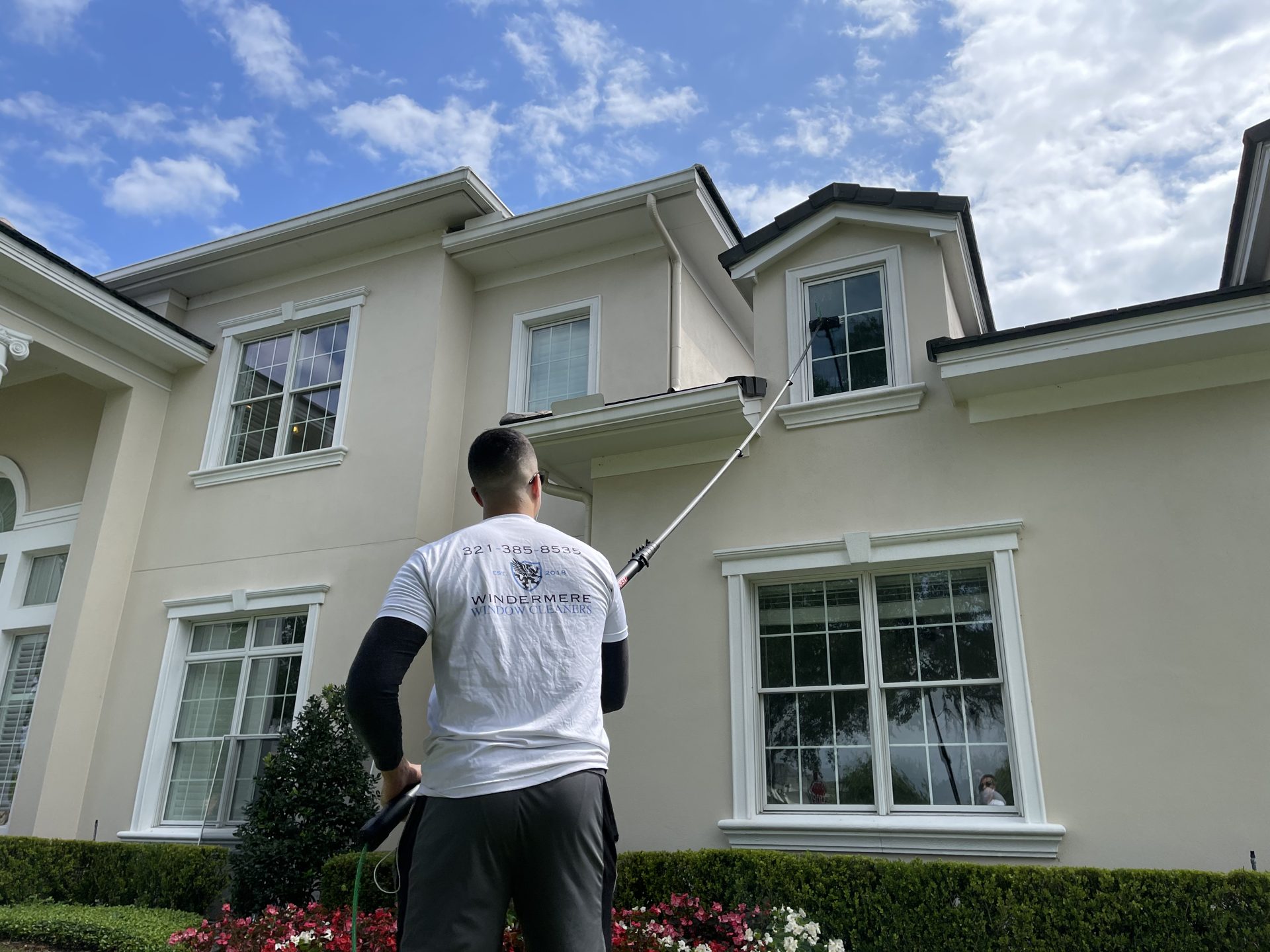 Residential window cleaning: technician cleaning second-story windows of a luxury home with a water-fed pole