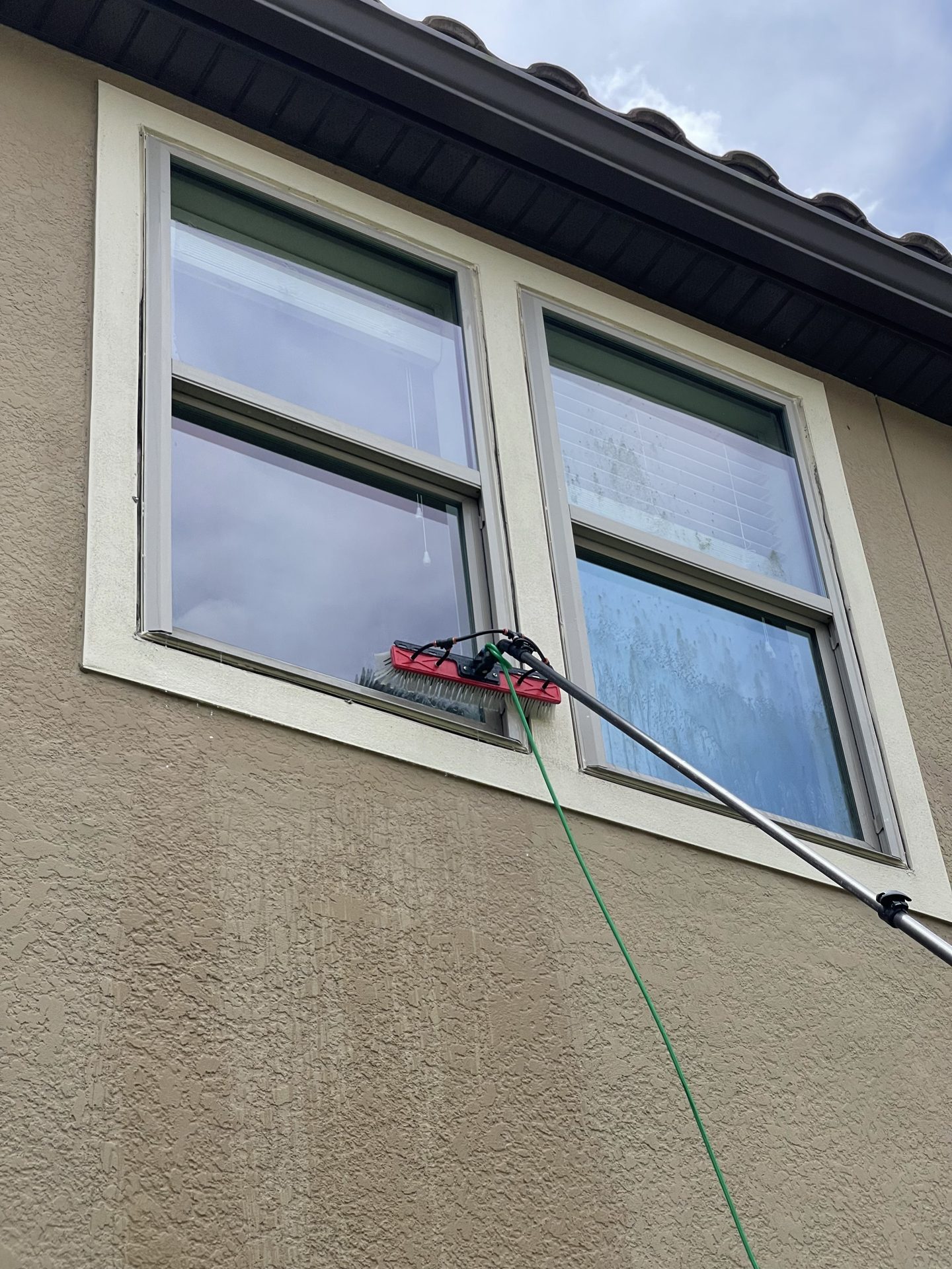 Technician cleaning second-story windows of a home with a water-fed pole