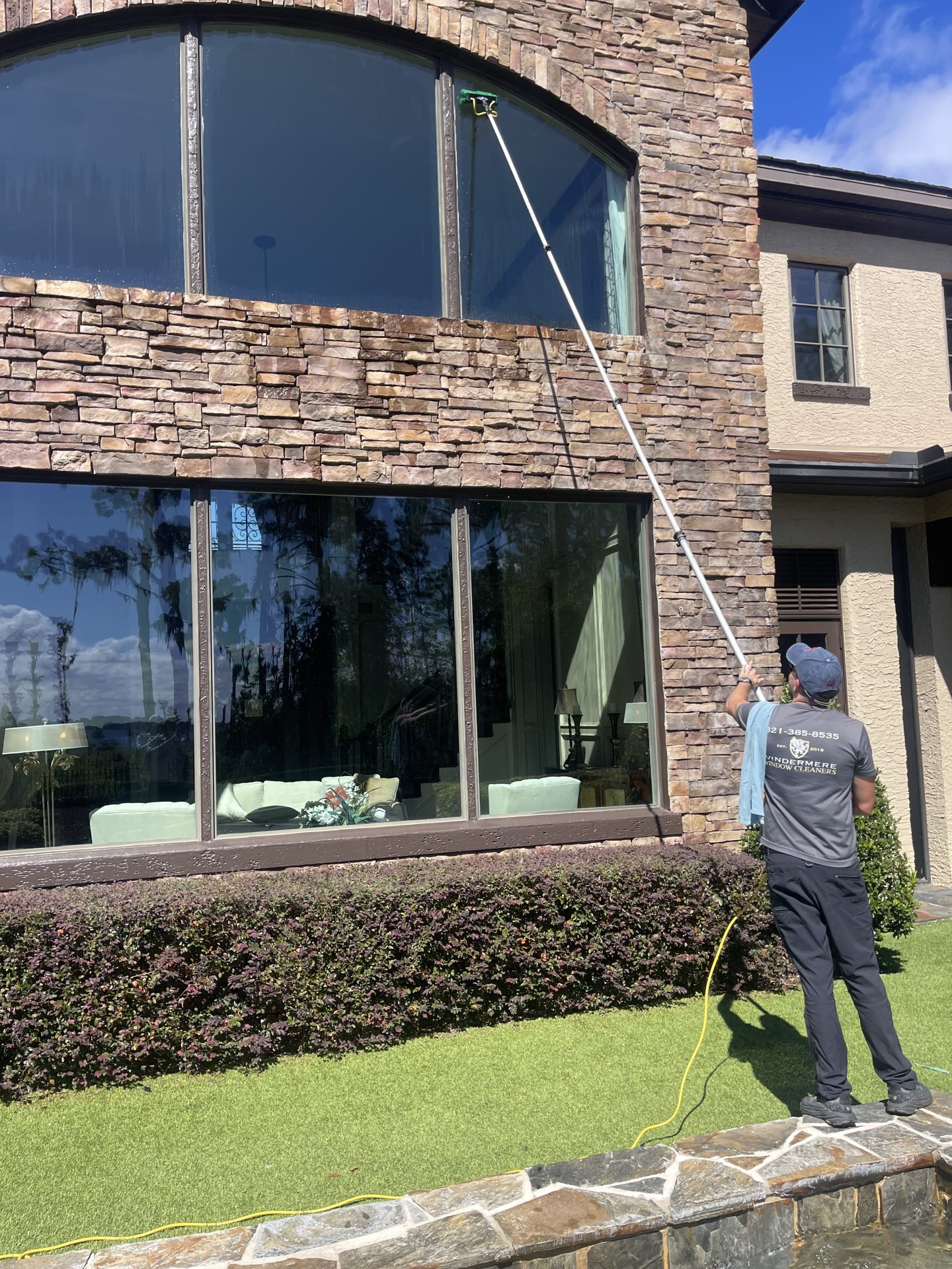 Water-fed pole cleaning of an arched window on a stone-front home