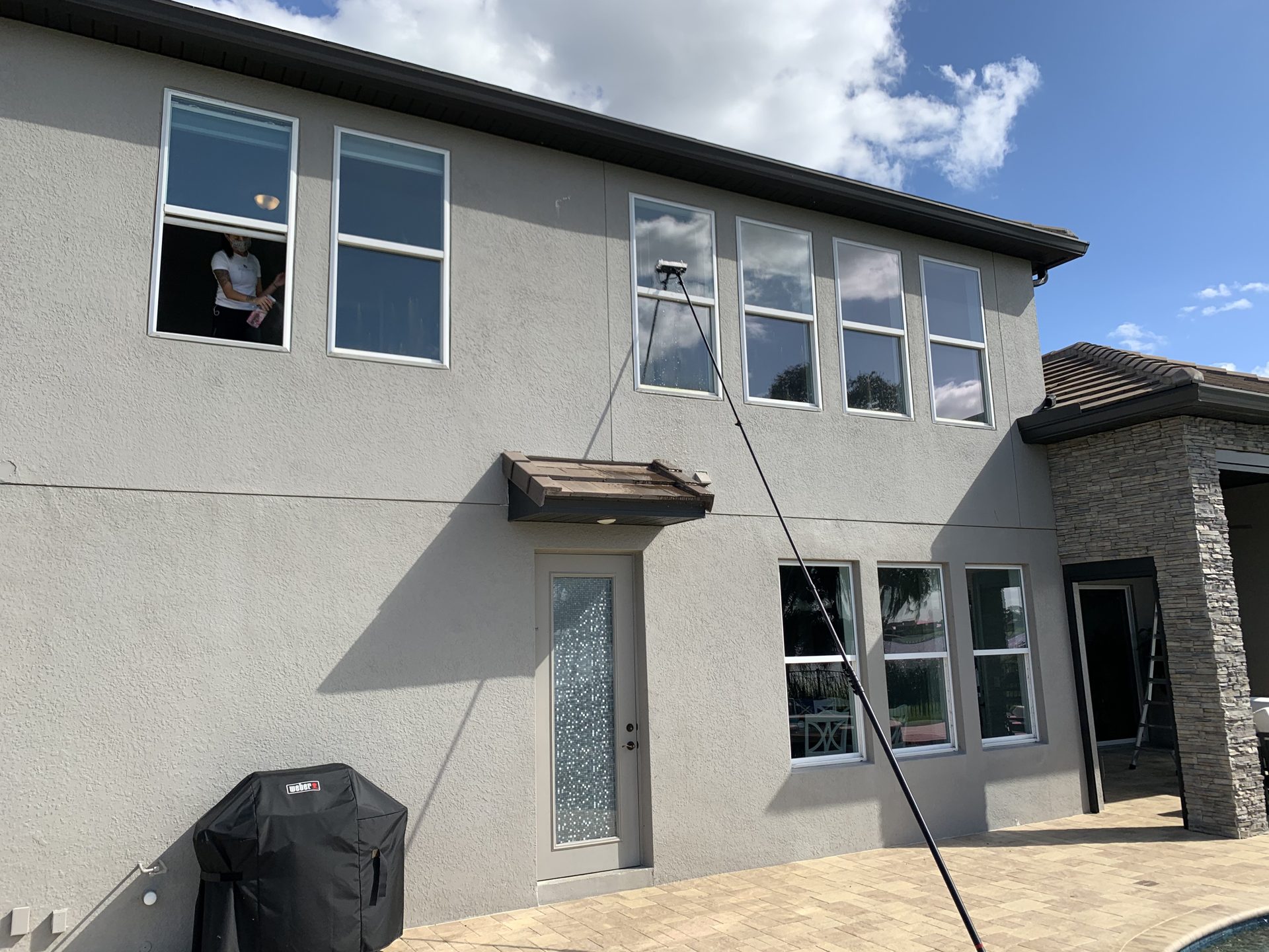 Technician cleaning the rear windows of a two-story home