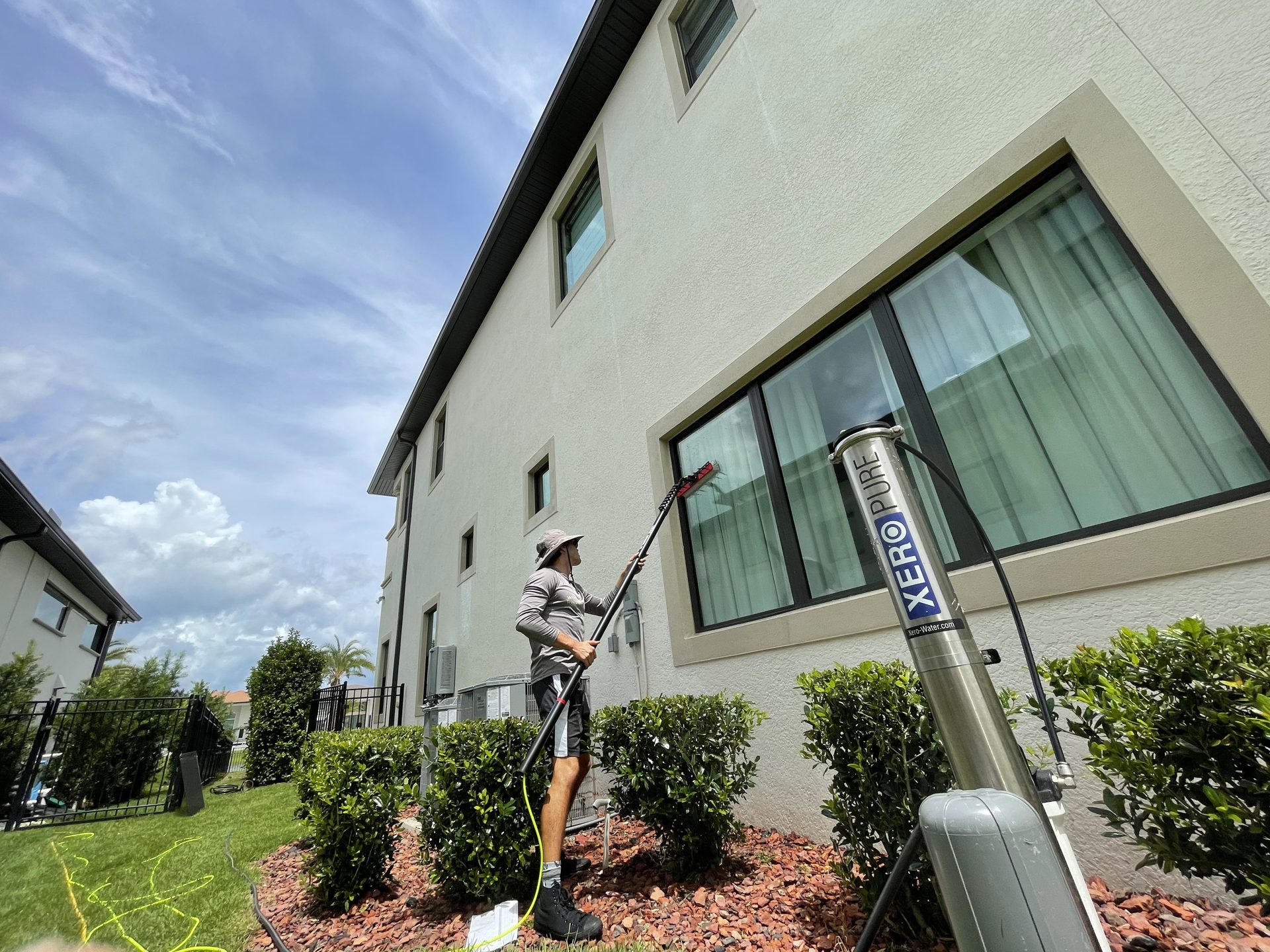 Technician cleaning second-story windows of a home using a pure water system