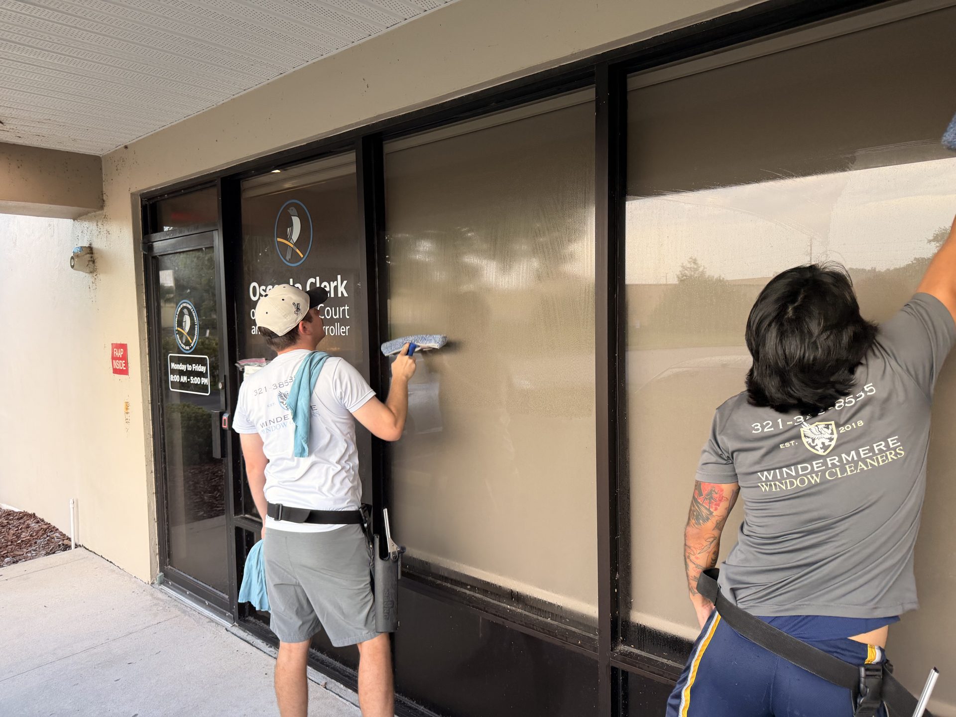 Two technicians hand-cleaning a storefront's glass wall