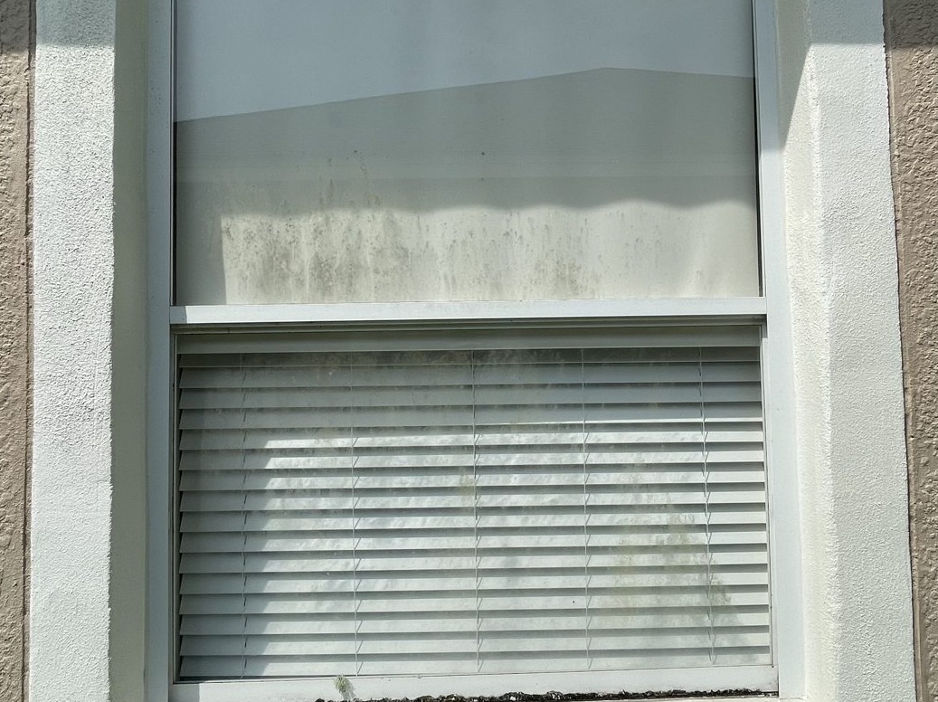 The same home window before cleaning, with dirty blinds and dulled glass